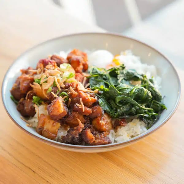 A brunch bowl from Take Ur Seat with rice, braised chicken, spinach, and a poached egg.
