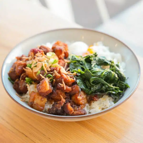 A bowl of Take Ur Seat's brunch with rice, braised pork, greens, and a fried egg.