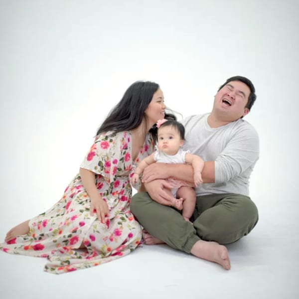A family of three, a mother, father, and baby, sitting and laughing together.