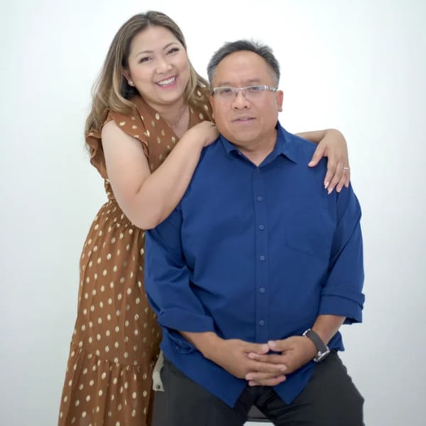 A smiling woman in a brown polka dot dress with her arm around a man in a blue shirt.