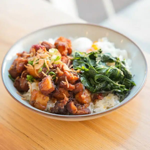 A bowl of rice topped with braised pork, green vegetables, and a poached egg.