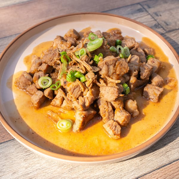 Close-up of Take Ur Seat's brunch dish featuring diced meat in sauce, garnished with green onions and fried shallots.