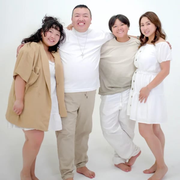 Four smiling people, two men and two women, stand arm-in-arm against a white background.