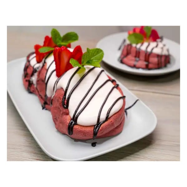 Two plates of red velvet pancakes topped with whipped cream, chocolate drizzle, strawberries, and mint.