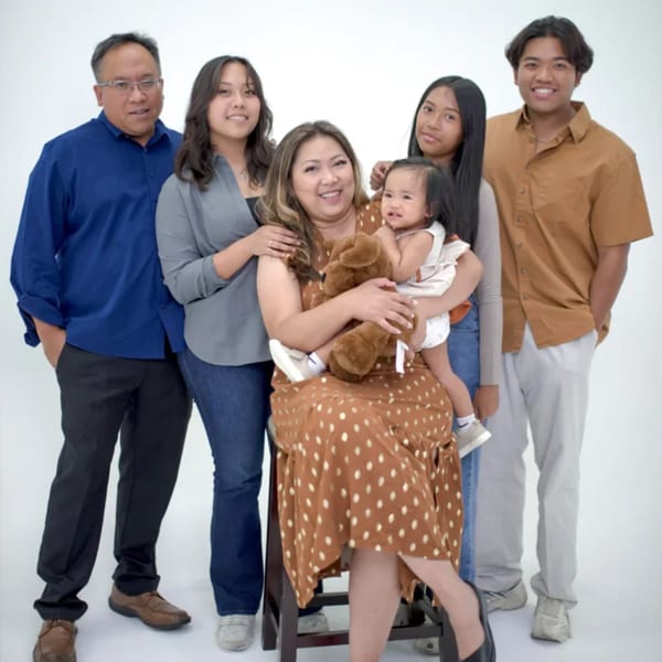 A family of six, including a baby, poses together against a white background.