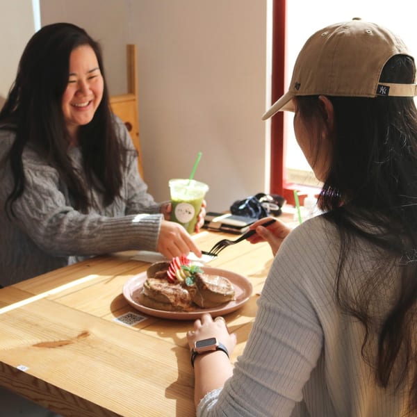 Two women enjoying brunch, with one eating pancakes and the other holding a green drink.